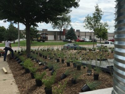 Several plant pots lined up on soil to be planted next to a large industrial metal cistern.