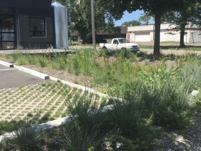 A black building in an industrial architectural style with a rain garden full of plants and permeable parking spots in the foreground.