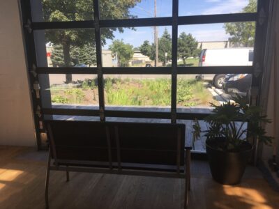 A view from inside an industrial building with a garage door, looking out into the rain garden.