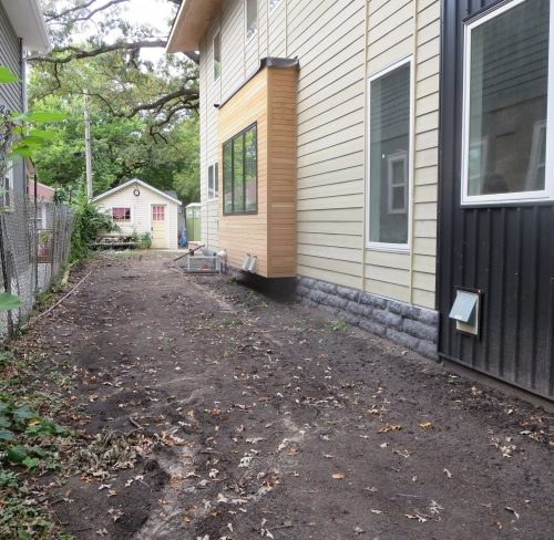 The narrow side of a black and natural wood modern home with completely bare dirt and.