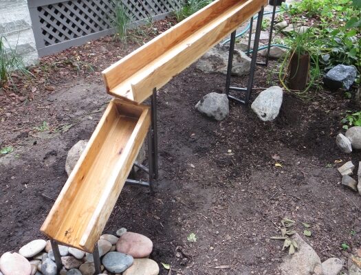 A three tiered wooden water chute leading to a rocky creek.