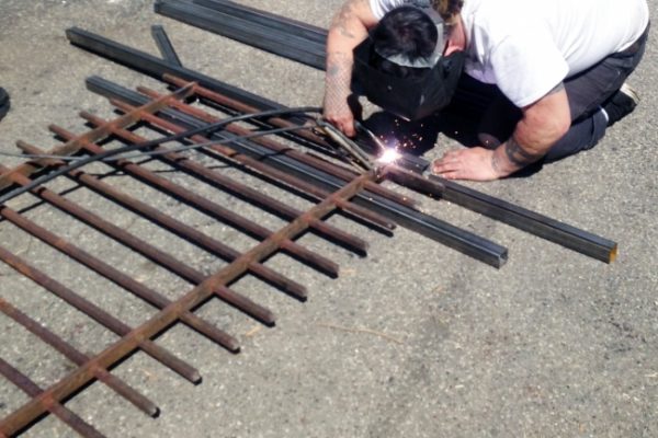 A welder making a custom metal fence on concrete ground.