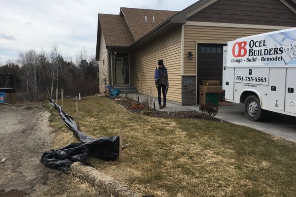 A patchy short front lawn of a beige suburban home butting up next to a bare lawn under construction.