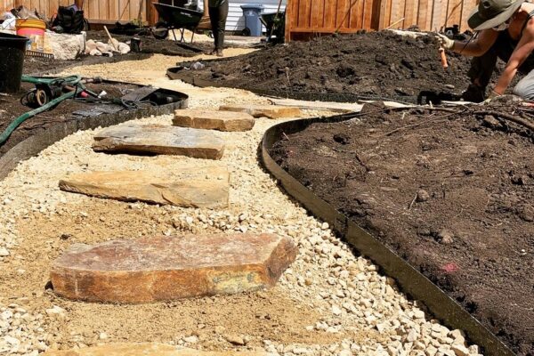 Laid natural stone on a gravel path as it is being installed for the new backyard oasis.