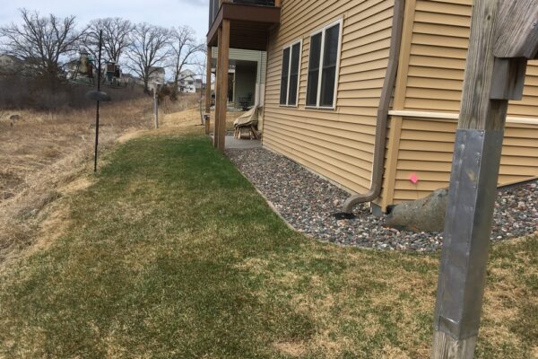 A patchy dry grass lawn to the left of a beige suburban home.