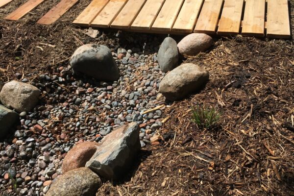 A simple wooden bridge and pathway over a rocky dry creek in a backyard.