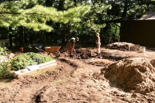 Surrounded by a stripped yard and piles of amended soil, members of the the Light Dark landscape installation crew dig the large rain garden basin, prepping the ground for the water reclamation garden.