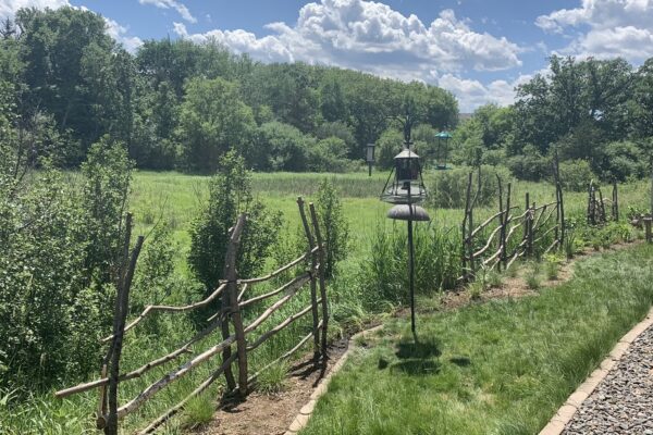 A textured grassy backyard butting up next to a wetland with a rustic wooden fence and bird feeders on a sunny summer day.