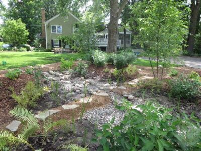 A dry rocky creek bed with a stone path running through it and a light green house in the background.