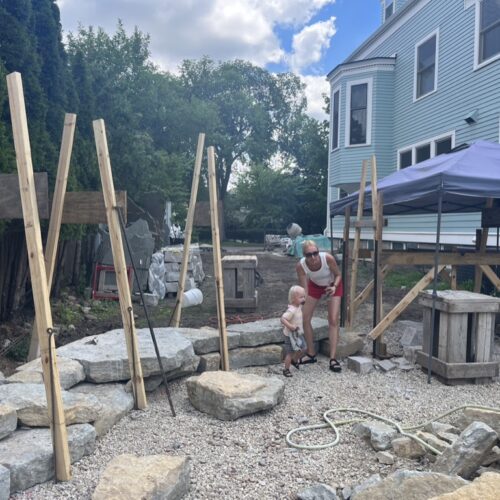 Wooden boards in an a-frame formation act as temporary guides for a in-progress dry-stacked stone wall.