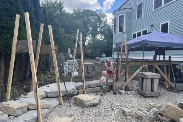 Wooden boards in an a-frame formation act as temporary guides for a in-progress dry-stacked stone wall.