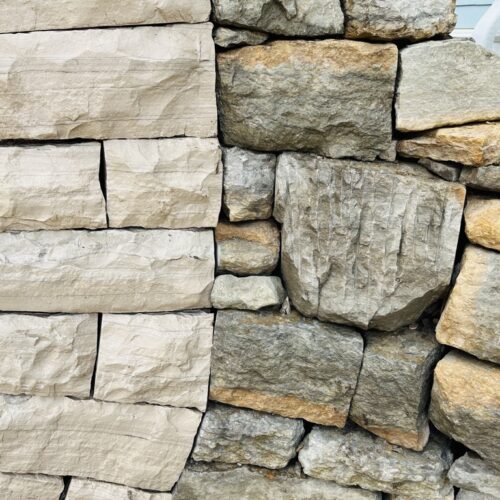 A close up detail of the connection between a multi-colored dray-stacked stone wall and a buff colored limestone moon gate.