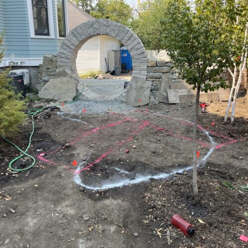 In an unfinished garden, overlapping outlines of white and pink spray-paint delineate the layout for a future rain garden basin and wood boardwalk.