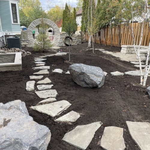 An empty side yard in the Kenwood Ave Neighborhood of Minneapolis has been transformed into a woodland retreat with the addition of newly planted birch trees, large gray boulders and a buff stone stepper path.