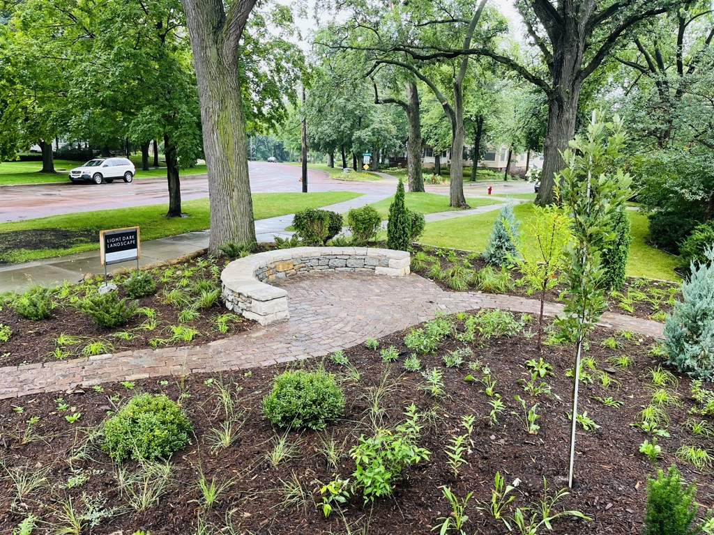 A newly constructed cobblestone path meanders through a freshly planted prairie garden toward a semi-circular stone seating circle, situated in a private front yard in the traditional and affluent Kenwood neighborhood of Minneapolis.